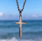 Polished silver tone cross pendant with the sea in the background
