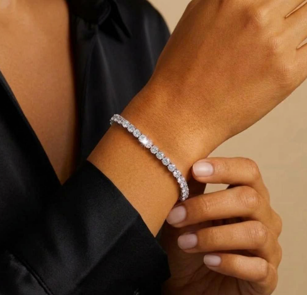Silver tone tennis bracelet shown on a wrist beside a black sleeve