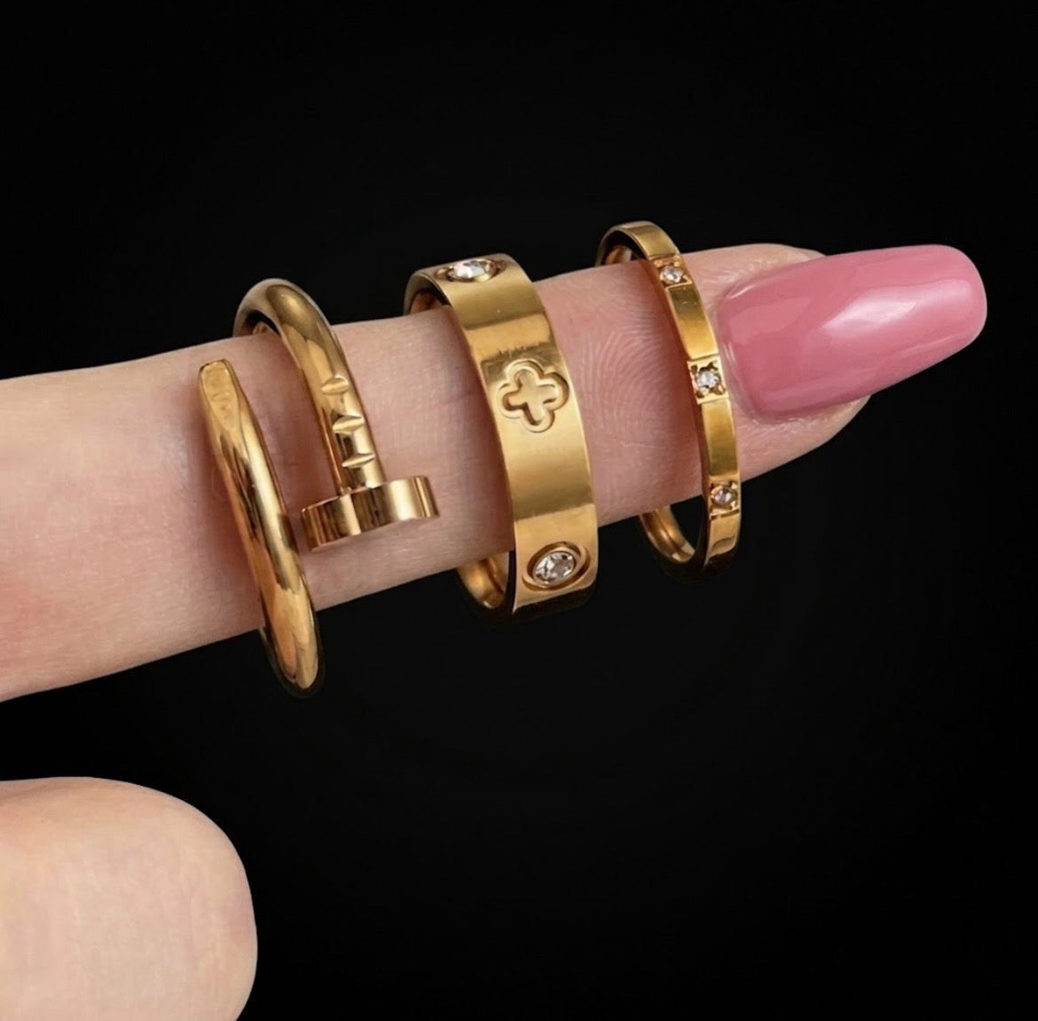 Three gold tone rings with nail-inspired, clover and stone details on a finger
